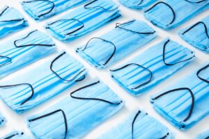 Rzędy niebieskich maseczek ochronnych ułożonych na białym tle, symbolizujące listę pilnych potrzeb, które ujawniły skalę problemów w polskich DPS-ach podczas pandemii.