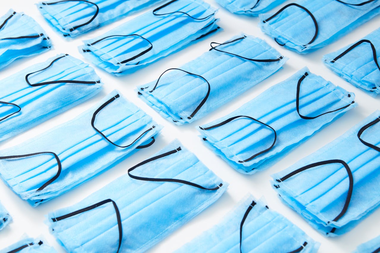 Rzędy niebieskich maseczek ochronnych ułożonych na białym tle, symbolizujące listę pilnych potrzeb, które ujawniły skalę problemów w polskich DPS-ach podczas pandemii.